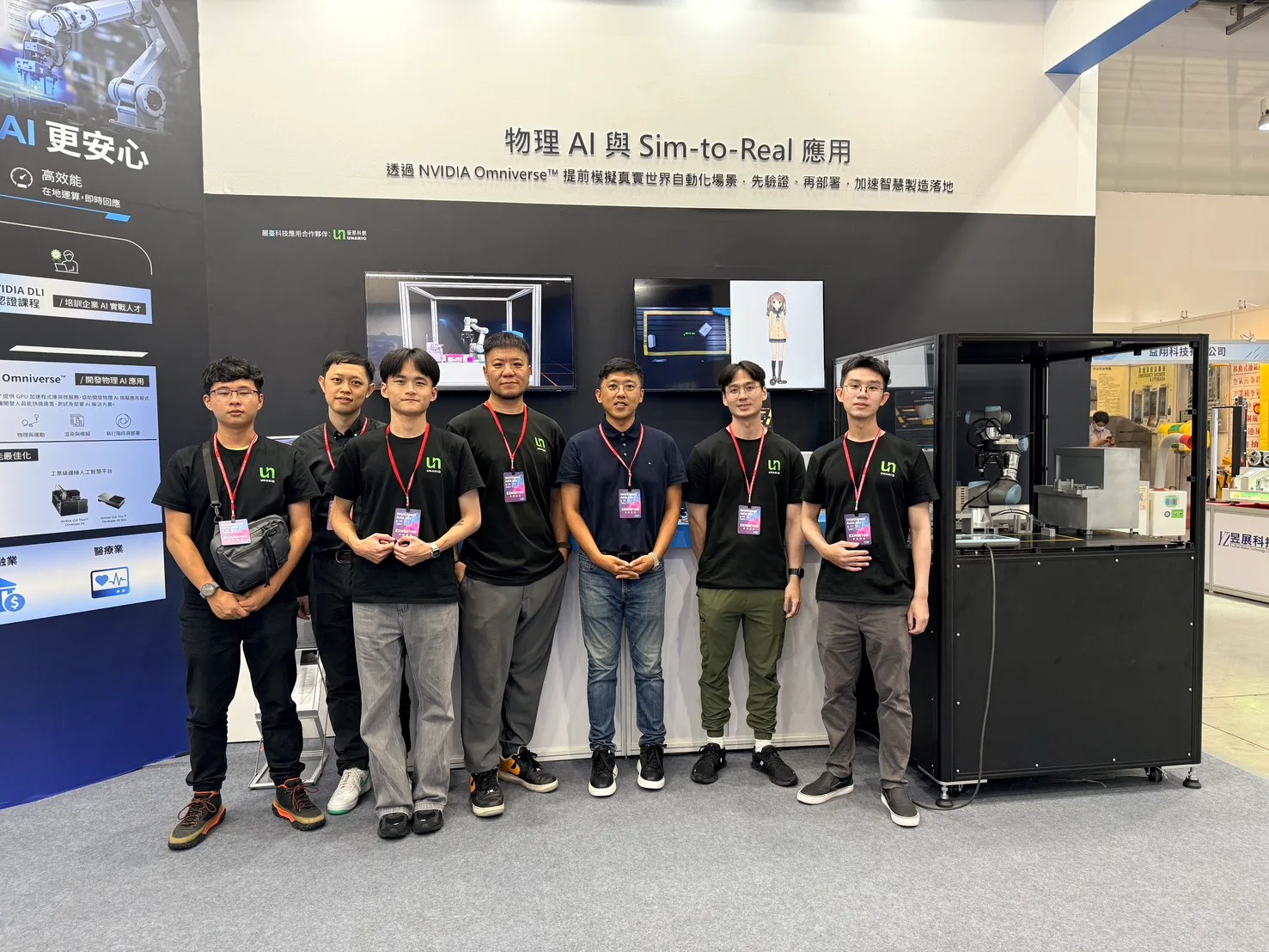 優那科創團隊於 2026 台北國際自動化工業大展攤位前合影，背後主視覺牆寫著「物理 AI 與 Sim-to-Real 應用」與 NVIDIA Omniverse 模擬說明，右側為玻璃防護罩內的協作型機器手臂實機